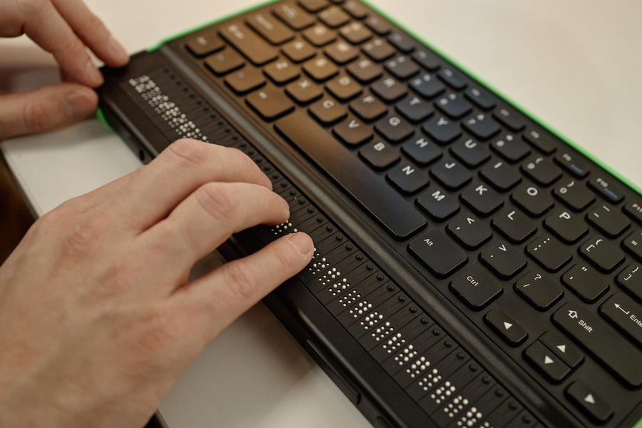 Hands reading a refreshable braille display integrated with a computer keyboard
