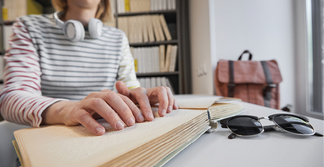 En person i ett biliotek läser en bok med blindskrift