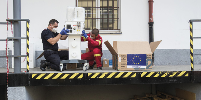 Dois trabalhadores montam um dispositivo médico numa plataforma de carga. Ao lado deles, há uma caixa com a bandeira europeia.