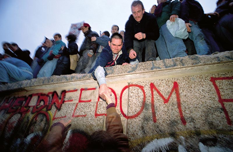 Jubelnde Menschen feiern auf der Berliner Mauer am Tag ihres Falls.
