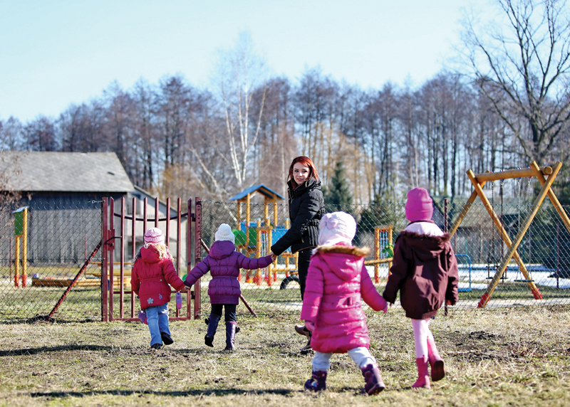 Młoda kobieta pilnuje dzieci na przedszkolnym placu zabaw