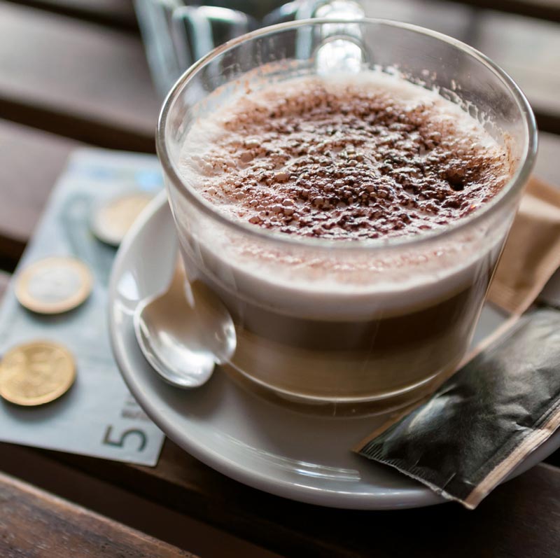 Skodelica kave na barski mizici ob evrskem bankovcu in kovancih
