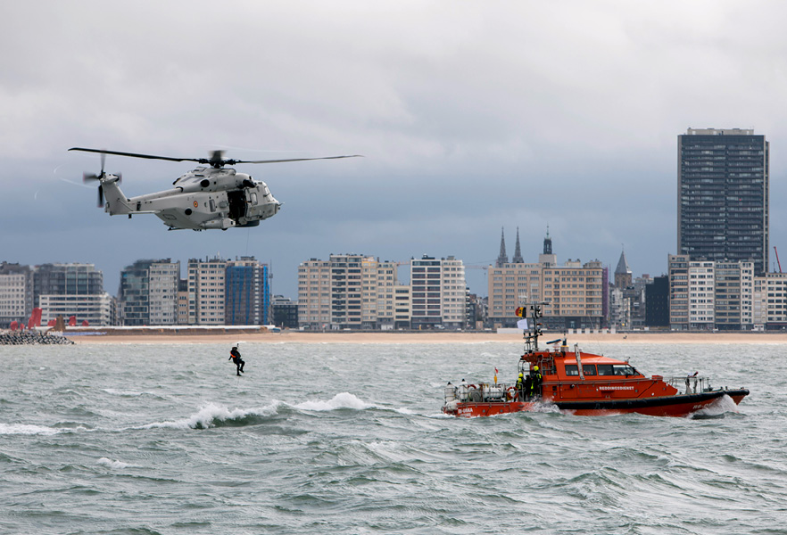 Achter een reddingsboot wordt een reddingswerker uit zee getild door een helikopter