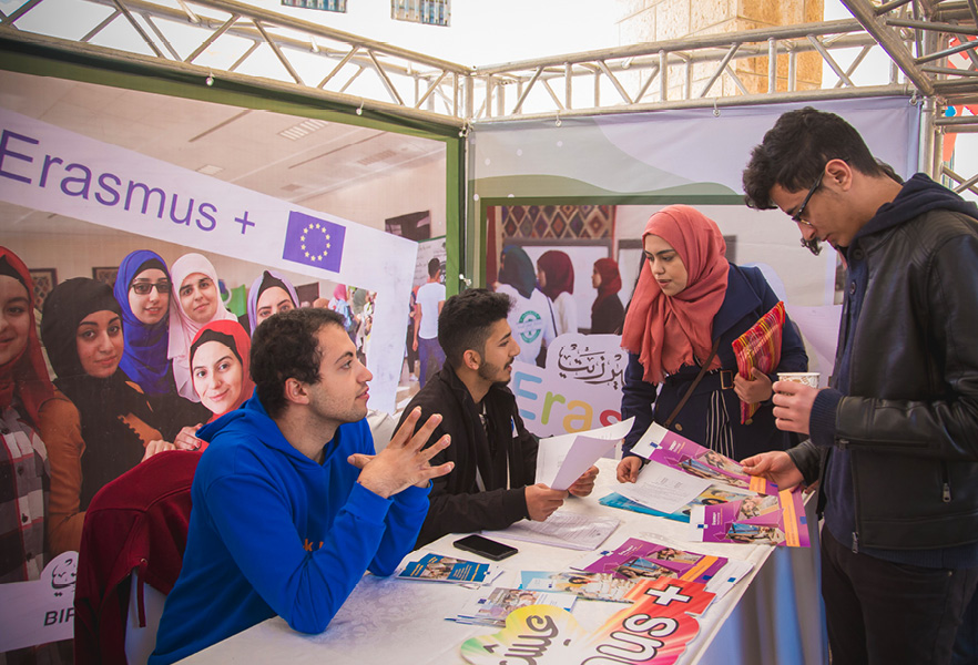 Ambasádori programu Erasmus+ sedia za stolom a odpovedajú na otázky iných študentov 