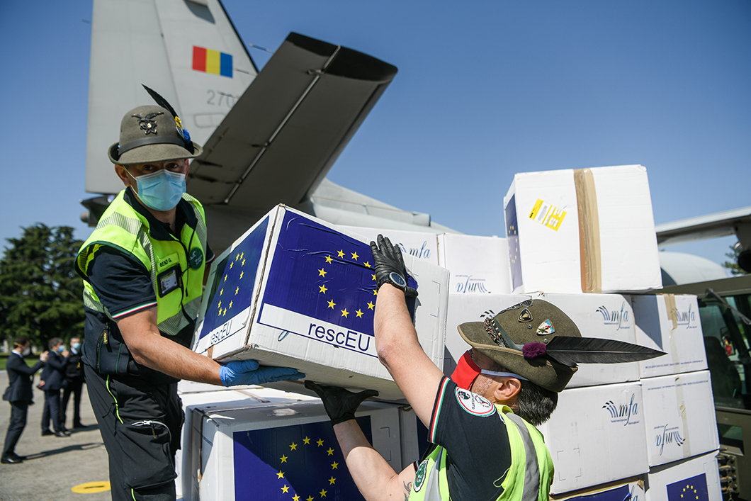 Two masked crisis workers unloading rescEU-branded boxes of masks from a small cargo plane.
