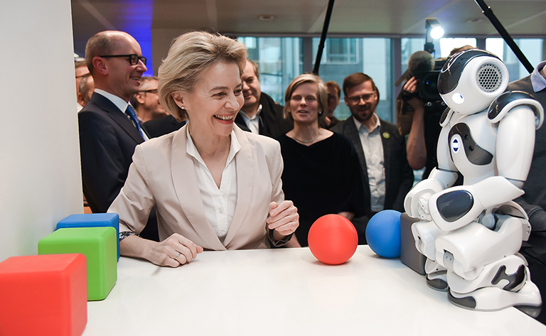 Ursula von der Leyen olha sorridente para um robô.
