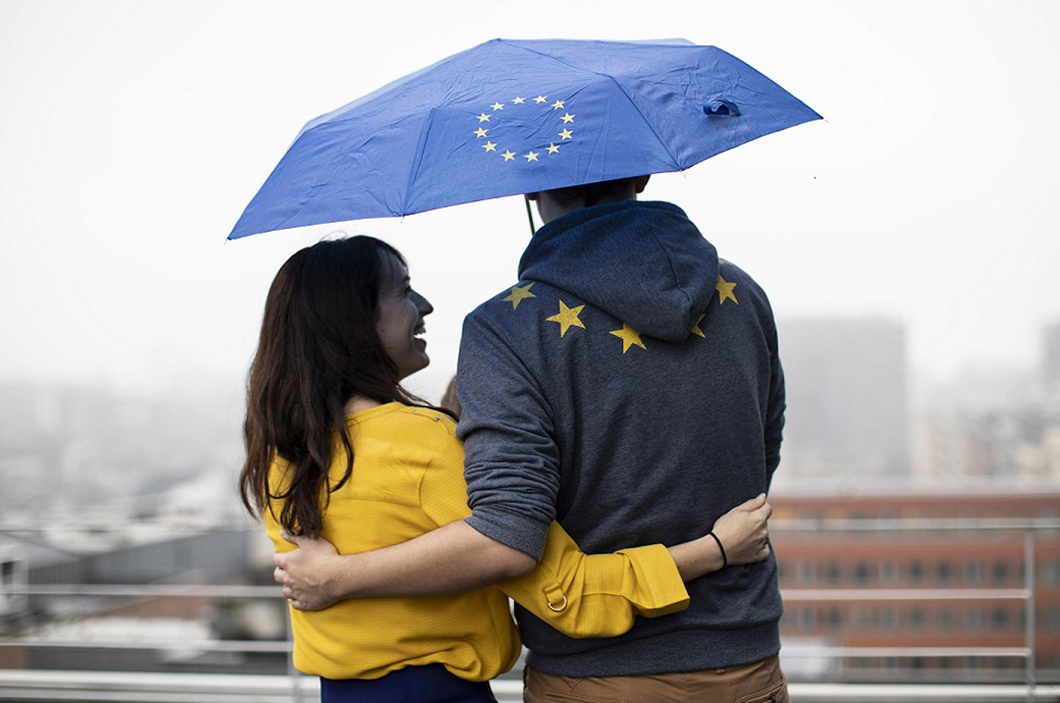 Two people sheltering under an umbrella with the EU flag on it.