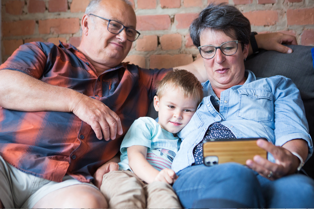 Two adults and a child sit on a couch and look at a smartphone together.