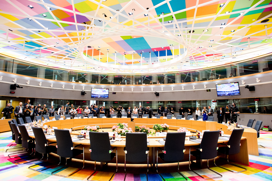 Fotografie cu sala de reuniune a Consiliului European în care se văd persoane în fundal.