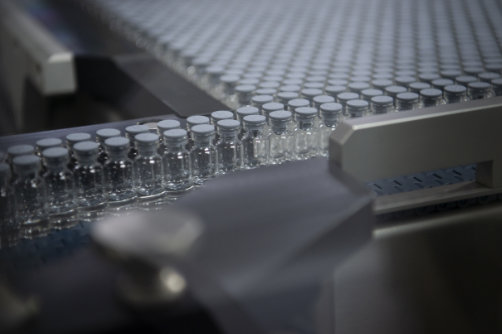 A close-up of medical vials on a conveyer belt waiting to be filled.