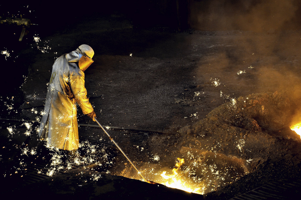 A worker in protective gear stokes a fire inside a blast furnace.