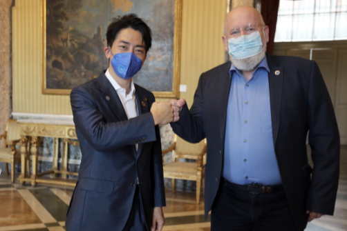 Frans Timmermans et Shinjirō Koizumi, masqués, se saluent poing contre poing, devant l’appareil photo.