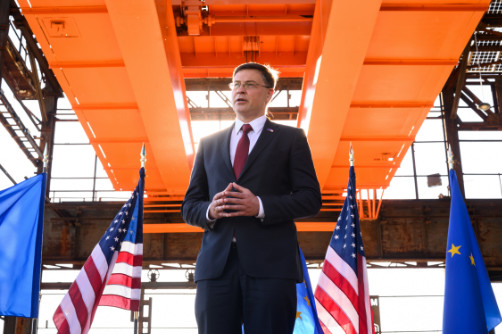 Valdis Dombrovskis houdt een toespraak; op de achtergrond een rij om en om geplaatste vlaggen van de EU en VS.