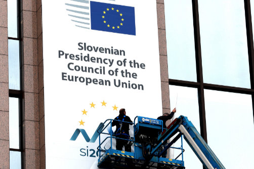 A worker on a platform hoist smoothing out a banner on the side of a building.