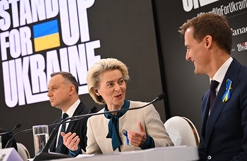 Andrzej Duda, Ursula von der Leyen ja Hugh Evans istuvat puhujalavalla rinnakkain ”Stand Up for Ukraine” -julisteen edessä.