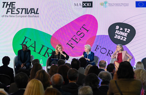 Ursula von der Leyen talar med publiken vid en paneldiskussion med Diébédo Francis Kéré, Monica Maggioni och Giovanna Melandri framför Bauhausfestivalens bakgrundsillustration.