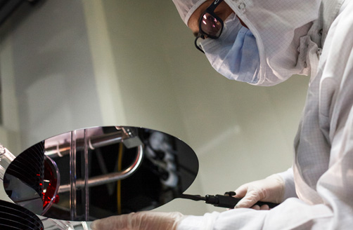 A worker in a protection suit examining a silicon wafer.