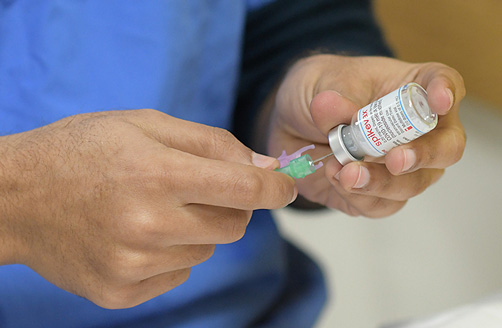 En manlig vårdgivare drar ut en dos covid-19-vaccin ur en flaska med en injektionsspruta.