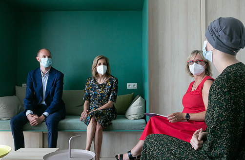 Stella Kyriakides wearing a mask, sitting and talking to a hospital patient during a visit.
