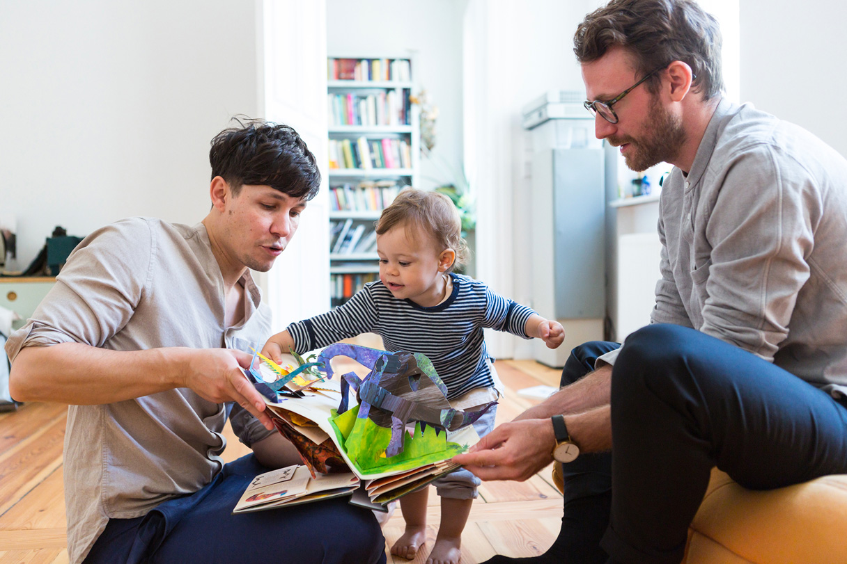 Divi vīrieši mazam bērnam lasa priekšā pasaku grāmatu.