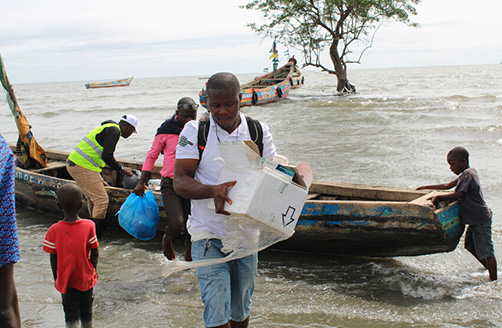 Trys vaikų stebimi vyrai Siera Leonėje iš medinės valties iškrauna medicinos priemones.