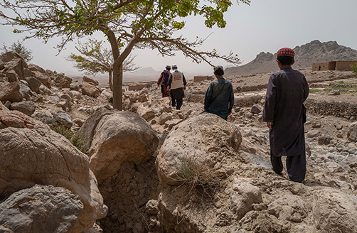 Vier mannen lopen door een droog, rotsachtig landschap.