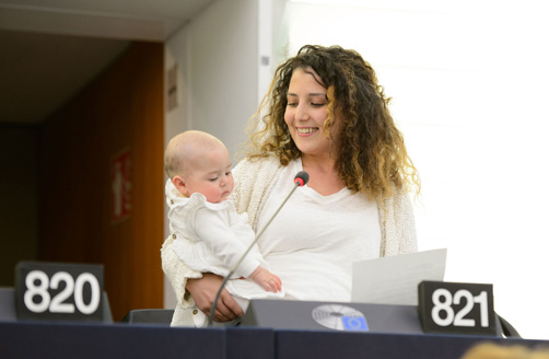 A young mother holding her baby while delivering a speech at a lectern.