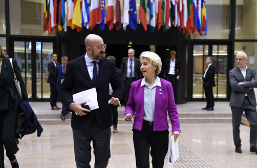 Ursula von der Leyen și Charles Michel merg spre cameră având în fundal drapelele statelor membre ale UE.
