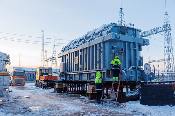 Ein Stromaggregat wird in einem verschneiten Industriegelände auf einen Lastkraftwagen geladen.