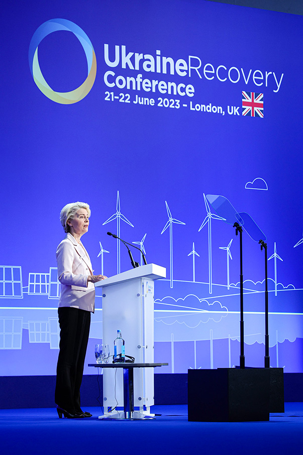 Ursula von der Leyen steht am Rednerpult und blickt ins Publikum. Hinter ihr ist auf einem großen Bildschirm „Ukraine Recovery Conference, 21st to 22nd June 2023, London, UK“ zu lesen.