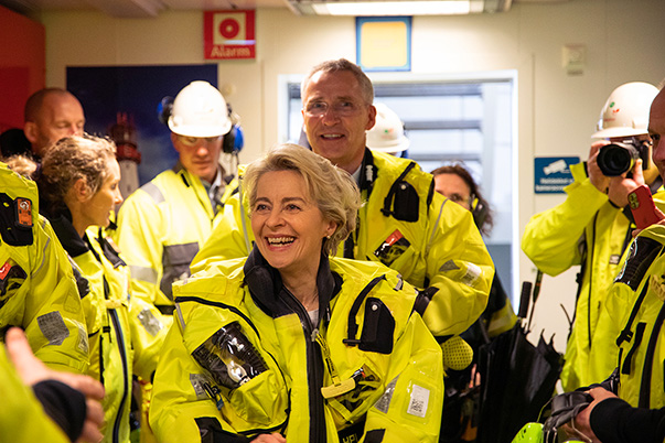Ursula von der Leyen und Jens Stoltenberg lächeln in die Kamera, umgeben von Mitarbeitern auf einer Bohrinsel; alle tragen neongelbe Warnjacken.