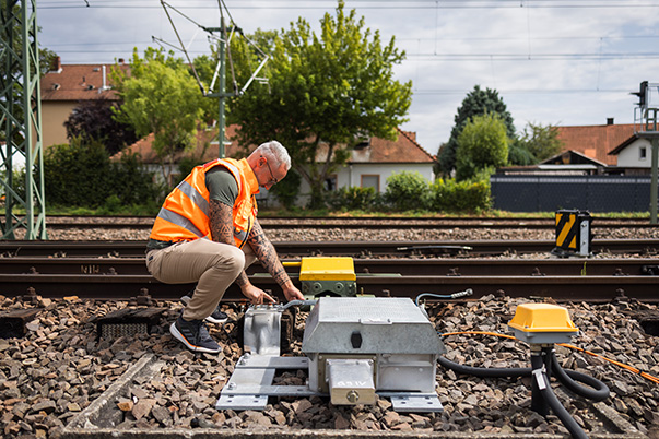 Ein Mann in einer Warnweste arbeitet mit Werkzeug an einer Eisenbahnstrecke.