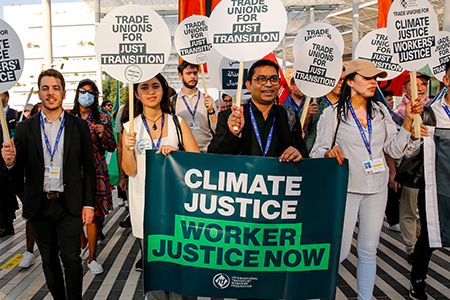Eine Gruppe von Menschen, die sich für Klima und Arbeitnehmergerechtigkeit einsetzt. Sie halten Schilder mit verschiedenen Slogans wie „Trade unions for just transition“, „Climate justice workers’ justice“ und „Climate justice worker justice now“.