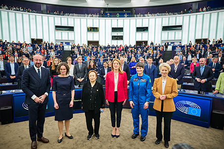 Charles Michel, Jessika Roswall, Shirin Ebadi, Roberta Metsola, Samantha Cristoforetti (in einem blauen Astronautenanzug) und Ursula von der Leyen stehen im Mittelpunkt eines großen Auditoriums, hinter ihnen stehen Menschen in Reihen an ihren Sitzplätzen.