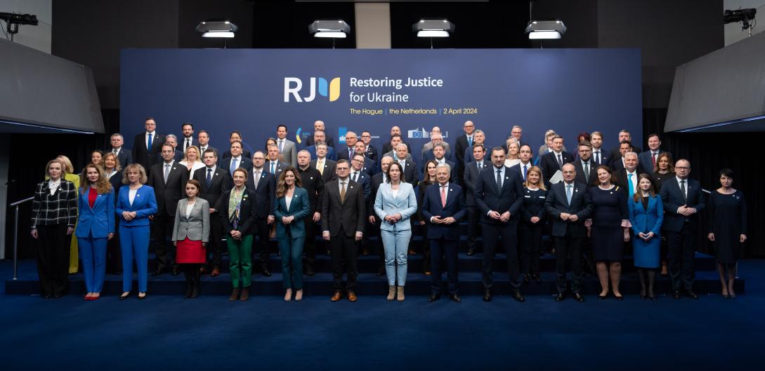 Eine große Gruppe von Personen posiert für ein Foto auf einem Podest vor einem Hintergrund mit der Aufschrift „Restoring Justice for Ukraine“ (Wiederherstellung der Gerechtigkeit für die Ukraine).