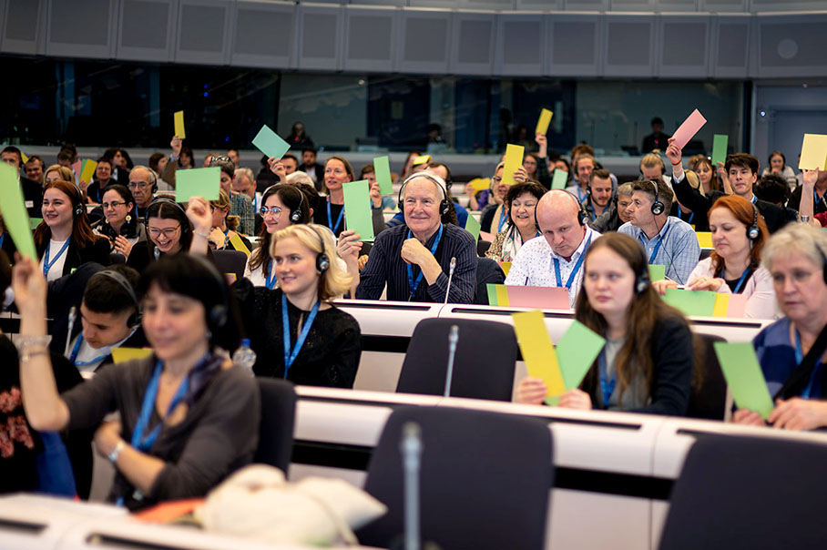 Ein Konferenzsaal, in dem die Teilnehmenden in Reihen sitzen und grüne und gelbe Karten hochhalten.