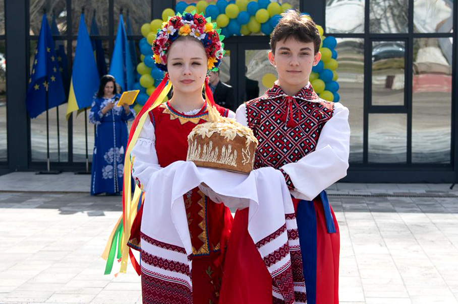 Un garçon et une fille en costumes ukrainiens traditionnels debout devant un bâtiment administratif neuf.