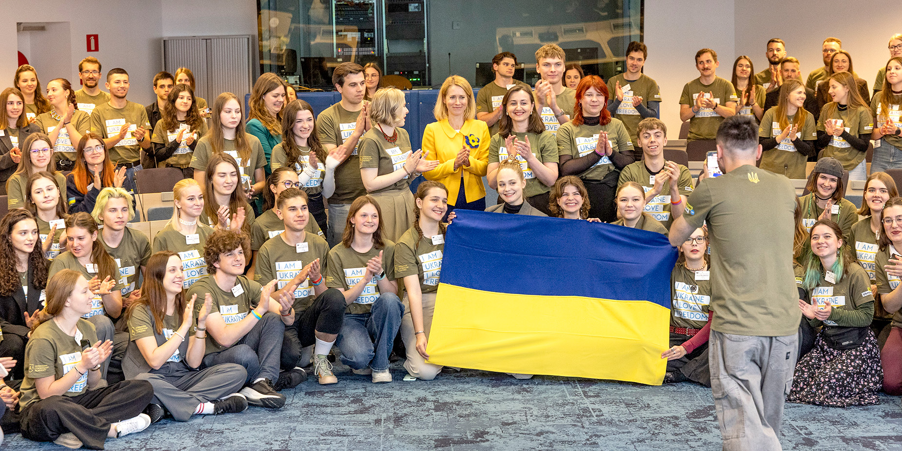 Un groupe d’étudiants ukrainiens rassemblés autour de Kaja Kallas et tenant un drapeau ukrainien.