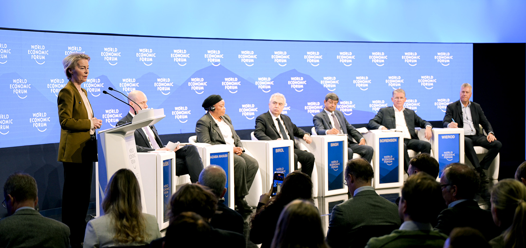 Ursula von der Leyenová má na pódiu prejav za rečníckym pultom. Na pódiu je s ňou ďalších šesť ľudí, ktorí sedia. V popredí vidno publikum sediace čelom k pódiu.