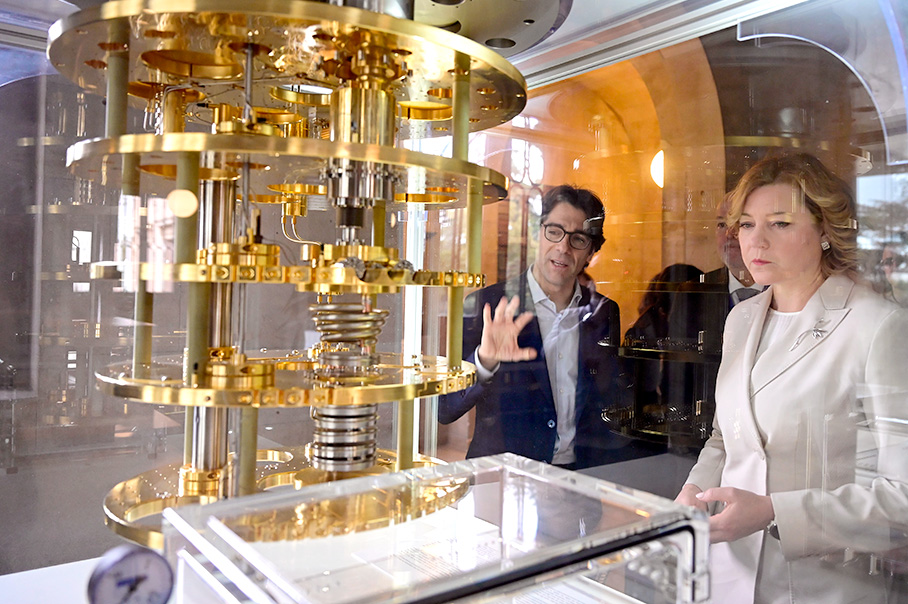 Henna Virkkunenová pozoruje kvantové výpočtové kryostatické zariadenie zlatej farby s vrstvenými kovovými komponentmi v sklenenom obale.