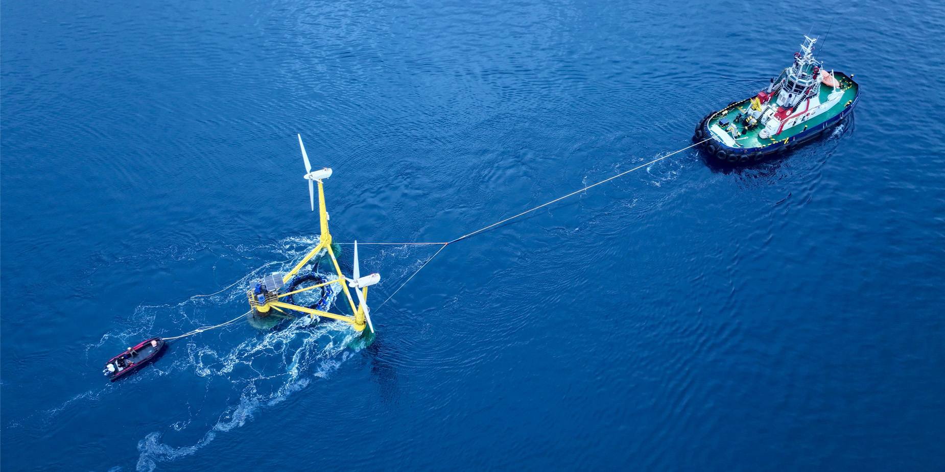 Twee boten slepen een innovatief prototype van een gecombineerde structuur van windturbines en aquacultuur naar zijn positie op zee.