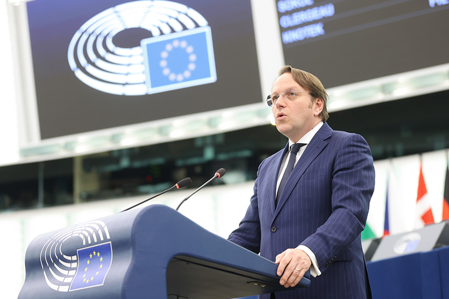 Olivér Várhelyi houdt een toespraak achter een lessenaar. Op de achtergrond hangt een groot bord met het logo van het Europees Parlement.