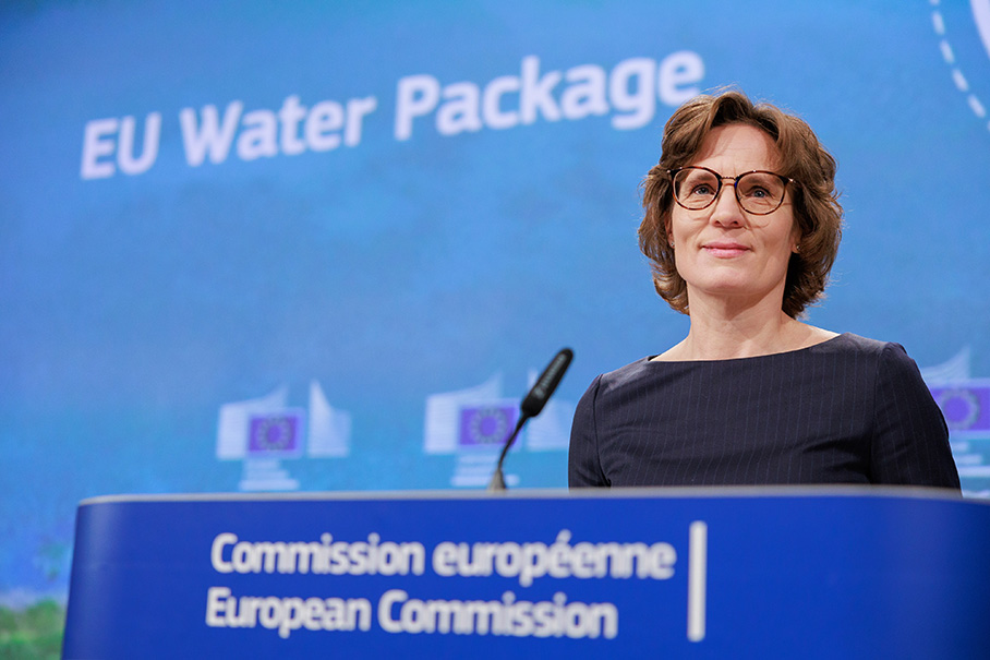 Jessika Roswall staat glimlachend op een podium voor een groot scherm met daarop de woorden “EU Water Package” (EU-waterpakket).