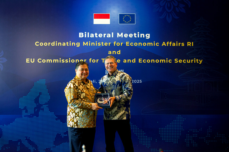 Марош Шефчович и Аирланга Хартарто са застанали заедно и се усмихват. И двамата носят типични за Индонезия пъстри ризи и държат кутия, в която има предмет с формата на цвете. На голям син екран на заден план най-отгоре са изобразени индонезийското и европейското знаме, а отдолу е изписано „Двустранна среща — координиращ министър по икономическите въпроси на Република Индонезия и комисар на Европейския съюз за търговията и икономическата сигурност“.