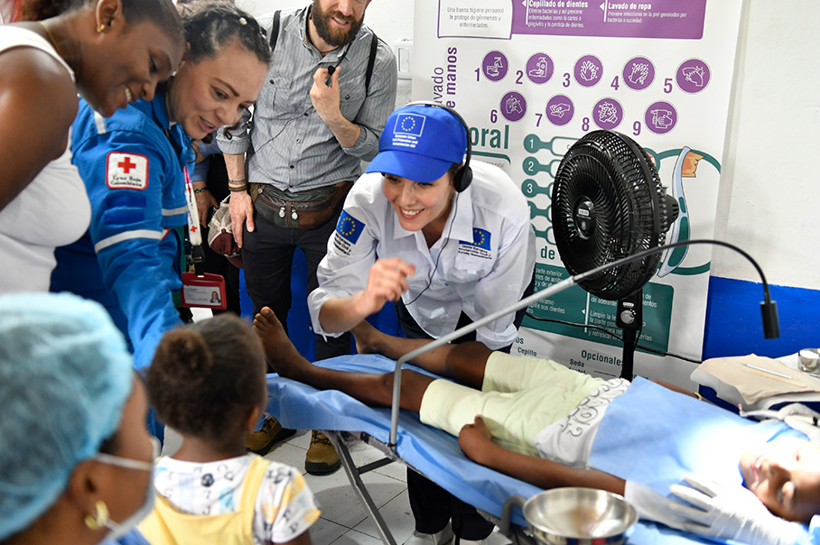 Хаджа Лабиб се усмихва и се е навела, за да говори с малко дете в медицинско заведение. Между тях друго дете лежи на зъболекарски стол.