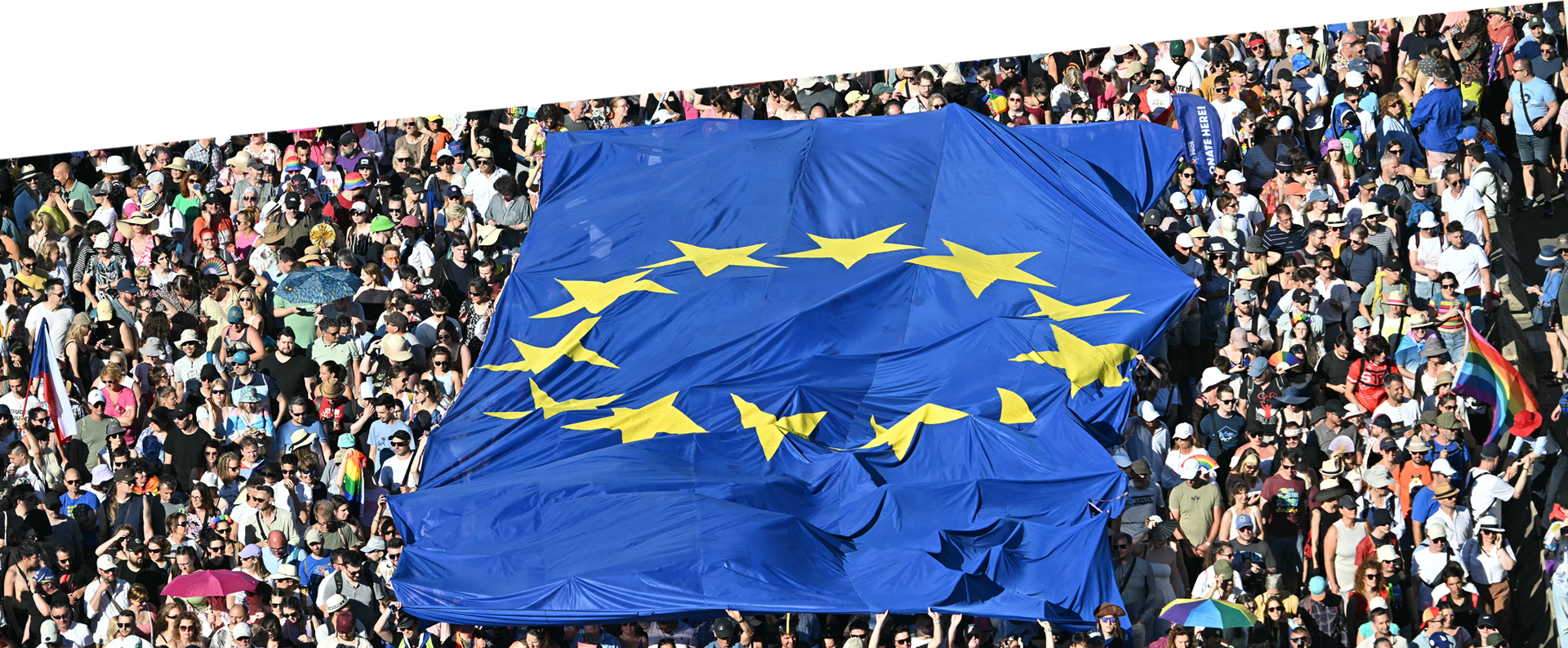 Ένα τεράστιο πλήθος που καταλαμβάνει όλη την εικόνα. Στο κέντρο, οι συγκεντρωμένοι κρατούν μια τεράστια ευρωπαϊκή σημαία.
