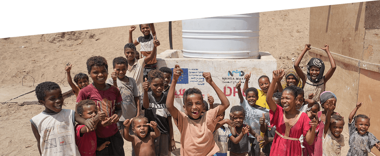 Група деца вдигат ръце и се усмихват пред резервоар за вода. Върху резервоара за вода се вижда частично закрито европейско знаме.