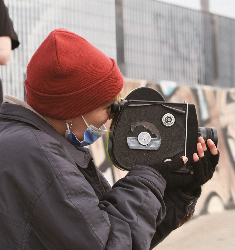 Una joven filmando con una cámara tomavistas antigua en un parque de patinaje.