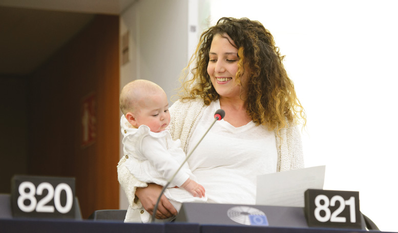 Женщина держит младенца во время выступления за кафедрой.