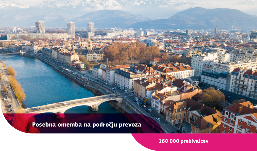 Zračni posnetek Grenobla s stavbami, reko s povezujočim mostom ter belimi gorami v ozadju